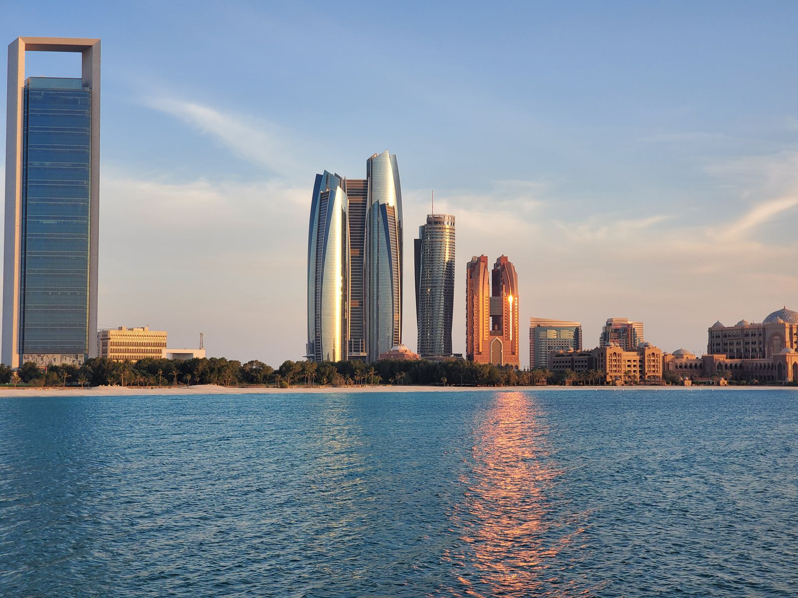 Abu Dhabi's skyline, including Emirates Palace, reflected in calm water at sunset