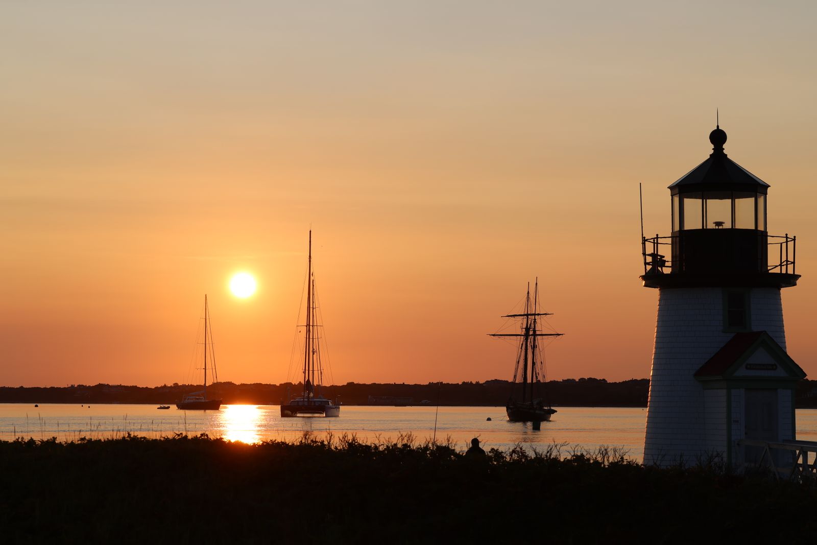 Sunrise over Brant Point Light and moored sailboats at the entrance to Nantucket Harbor